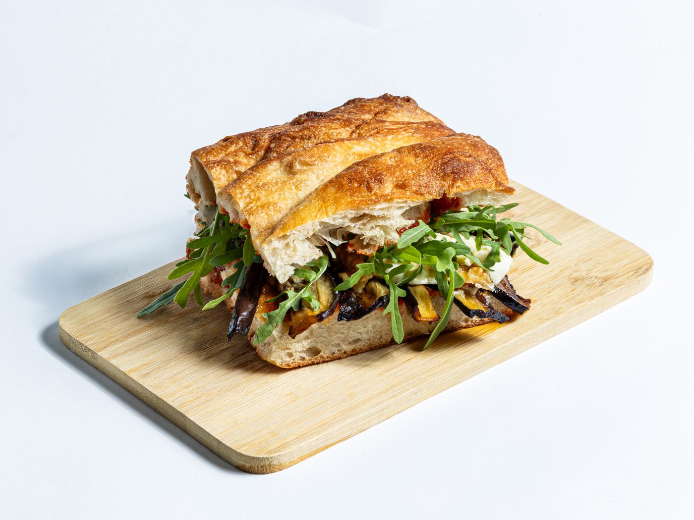 Belegte Focaccia mit gegrilltem Gemüse und Rucola auf einem Holzbrett